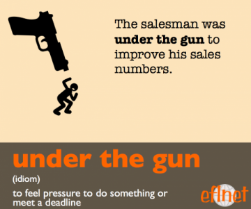 Under the gun. (Idiom) To feel pressure to do something or meet a deadline.